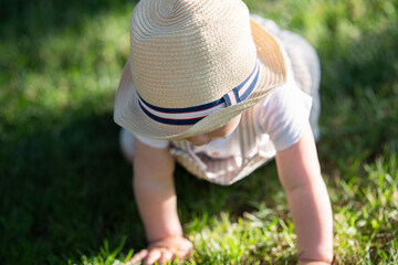 A baby with a hat on his head is sitting on the grass