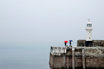 Para spacerująca pod parasolkami z psem nad morzem po nabrzeżu z latarnią 