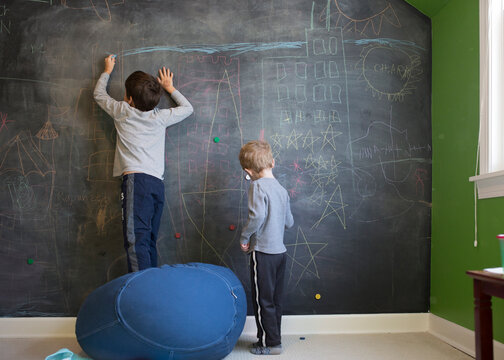 Rear view of brothers drawing with chalk on blackboard wall at home