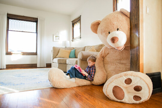 Side view of boy playing game while sitting on large teddy bear at home