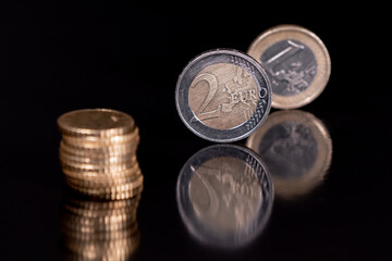 Euro coins isolated with pitch black background, reflecting in black metallic surface. Money on a very dark table.