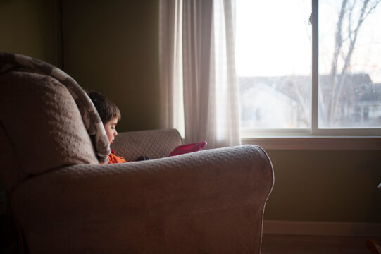 Boy playing with toy while sitting on chair by window