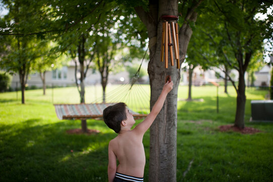 Shirtless boy playing with wind chime while standing at backyard