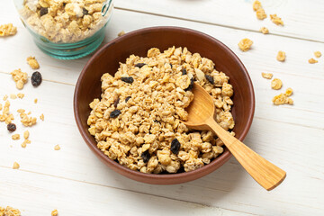 Healthy breakfast. Muesli with dried grapes in a clay bowl on a white wooden table. Muesli is scattered on the table.