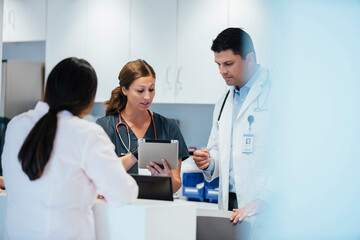 Nurse showing tablet computer to colleague with female doctor standing in foreground