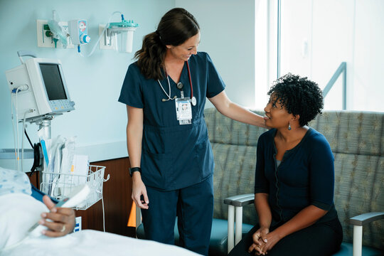 Cheerful nurse talking with woman while senior patient lying in hospital ward