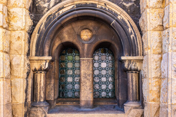 A stone wall with twin arched windows protected by green metal grates