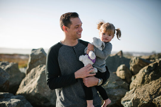 Portrait of cute daughter holding stuffed toy while being carried by father at beach