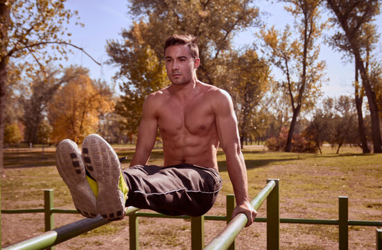 Shirtless man exercising on parallel bars at park