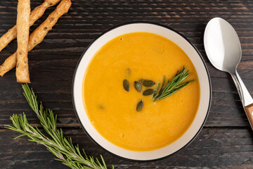 A bowl with pumpkin cream soup with grossini bread sticks and resemary on dark wooden background. Top view