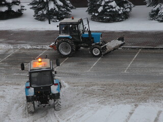 Two wheeled traktor machines cleaning a snow with scraper shovel blade on empty parking lot after...