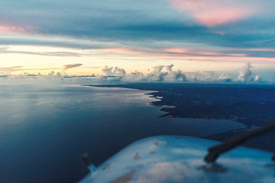 Cropped image of airplane flying over seascape against cloudy sky during sunset