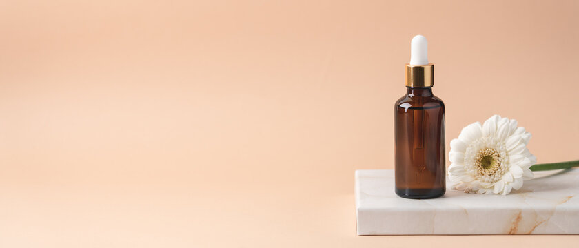 Cosmetic bottles with dark glass pipette on podium of marble boxes. Natural serum concept. Beige background