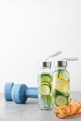 Lemon, cucumber and mint water in glass bottles. Sassy water for detox or dieting with fitness dumbbells in the background. Healthy eating, weight loss,  lifestyle concept