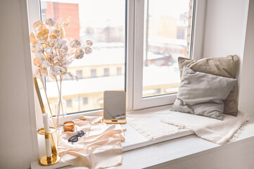 Fototapeta premium Cozy spring still life feminine scene golden shades. Female styled window sill minimalistic composition. Elegant accessories, mirror, sunglasses, earrings, dried flowers, candles, cozy pillows.