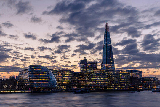 Low angle view of Shard London Bridge amidst illuminated city against cloudy sky during sunset