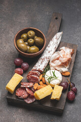 Variety of meat, cheese snacks, olives, grapes and nuts for wine. Dark background with copy space