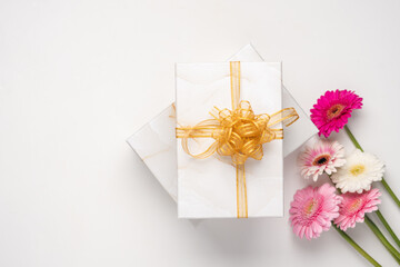 Two gift marble boxes tied with a golden ribbon and a bouquet of pink flowers on a white background. Gift and pink gerberas for festive day