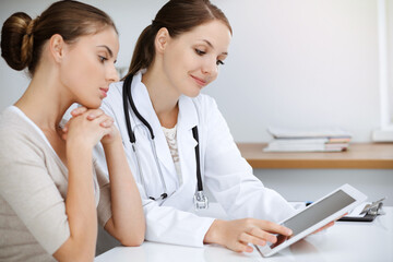 Doctor and patient are sitting and discussing health examination results while using tablet computer. Health care, medicine and good news concepts