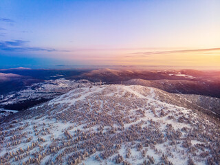 Colorful winter sunset in Sheregesh ski resort mountains covered trees. Aerial top view beautiful forest of Russia