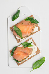 Salted salmon on whole wheat crisp toast with soft homemade cheese and spinach. Open sandwich on white background 