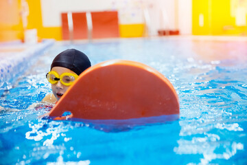 Happy little kid girl learning to swim with pool board with coach woman