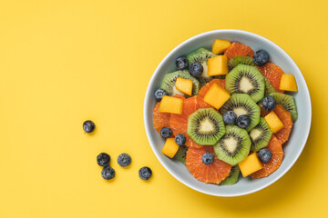 Fruit salad of red oranges, kiwi, mango and berries. Bowl of fruits on yellow background 