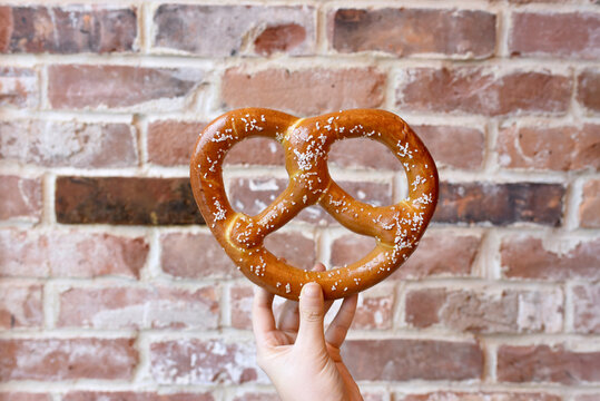 Cropped hand of person holding pretzel against brick wall