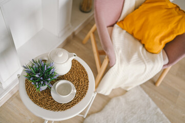 Stylish elegant eco composition living room with white breakfast table coffee cup teapot false fireplace dried flowers plants pampas grass pink powder armchair, blanket and pillow. Modern home decor