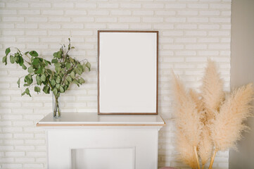 Stylish elegant eco composition of living room with white false fireplace, empty picture frame, dried flowers plants pampas grass. Modern home decor. Template. Mock up poster frame on the wall
