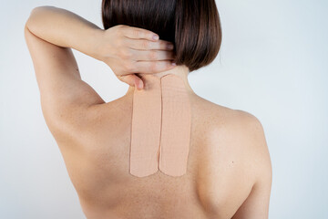 Kinesiology beige taping on the human back on a gray background with a copy space. Dynamic functional bandage taping on the girl's neck. Solution for back and neck pain. Headache.