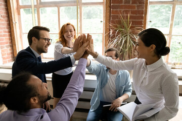 Excited diverse multiracial businesspeople give high five engaged in teambuilding activity at team...