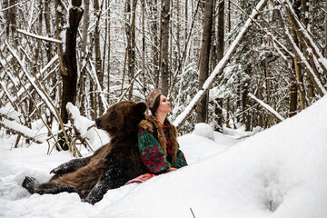 Russian beauty in folk national dress with a brown bear with a winter forest