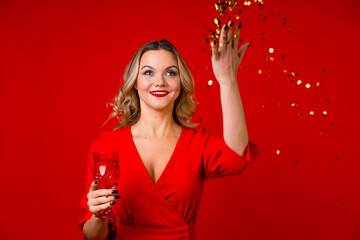 New year or holiday party, a young blonde in red drinks champagne and throws gold confetti.