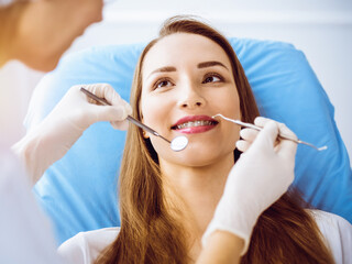 Smiling young woman with orthodontic brackets examined by dentist in sunny dental clinic. Healthy teeth and medicine concept