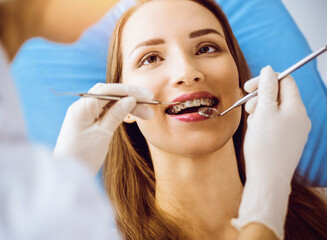 Smiling young woman with orthodontic brackets examined by dentist in sunny dental clinic. Healthy...