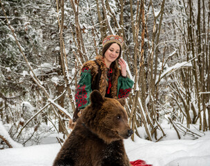 Russian beauty in folk national dress with a brown bear with a winter forest