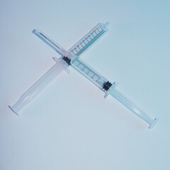 Two syringes. They are one over the other. Illuminated by neon light, blue and purple
