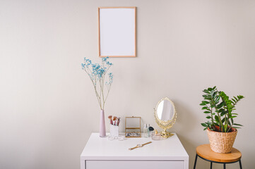 Minimalistic female still life workplace composition pastel colors. White table, empty poster mock up frame, stylish fashion accessories golden mirror. Home plant in eco wicker flower pot. Template.