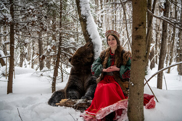 Russian beauty in folk national dress with a brown bear with a winter forest