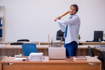 Young male furious employee holding baseball bat in the office