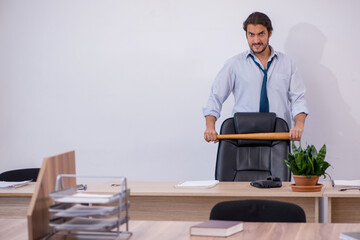 Young male furious employee holding baseball bat in the office