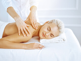 Fototapeta na wymiar Beautiful blonde woman enjoying back massage in spa center. Beauty and lifestyle