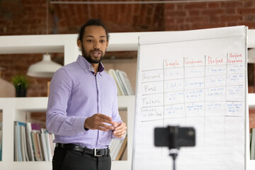 Motivated young African American male coach speak talk on video call on cellphone teaching online. Biracial man teacher have webcam virtual lesson or distant course using phone. Education concept.