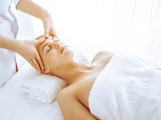 Beautiful blonde woman enjoying facial massage in spa center. Relaxing treatment in medicine and beauty concepts