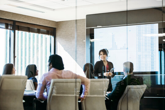 Businesswoman giving presentation in meeting seen through glass window