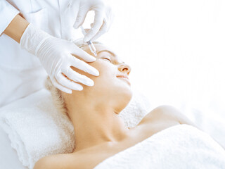 Beautician doctor hands doing beauty procedure to female blonde face with syringe in clinic. Cosmetic medicine and surgery, beauty injections concept