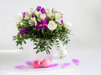 A beautiful Easter composition with a bouquet of flowers, pink painted chicken eggs and feathers on a white background.