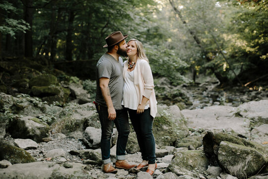 Side view of husband kissing wife while standing on rocks in forest