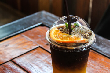 iced yuzu orange juice infused with espresso coffee decorating with sliced orange piece in plastic cup on wooden table in coffee shop cafe 